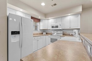 A modern kitchen with white cabinetry, a built-in microwave, a refrigerator, and a granite countertop. - French Quarter Resort | Family Condo Near Shows (Branson)