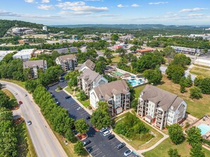 A residential area with multi-story apartment buildings, a swimming pool, and a road with vehicles. - Family Condo | Golf Discounts | Sleeps 8 (Branson)