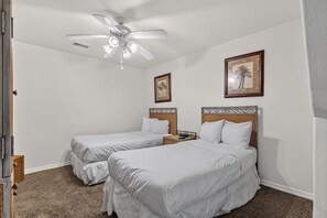 Ein Hotelzimmer mit zwei Einzelbetten, einem Deckenventilator und zwei gerahmten Bildern an der Wand.