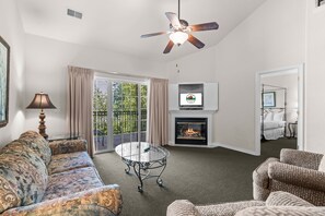 A living room with a sofa, armchairs, a glass coffee table, a fireplace, a ceiling fan, and a television. - Near the Branson Strip | 2BR + Loft Condo (Branson)