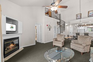 A living room with a fireplace, a television, a dining area with chairs, and a staircase. - Near the Branson Strip | 2BR + Loft Condo (Branson)