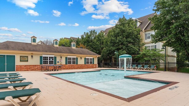 A swimming pool area with lounge chairs, a water fountain, and a building with a brick facade. - Pool • Hot Tub • 2BR + Loft | Branson Resort (Branson)