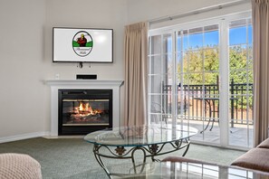 A living room with a fireplace, a glass table, and a balcony with a view of trees. - Pool • Hot Tub • 2BR + Loft | Branson Resort (Branson)