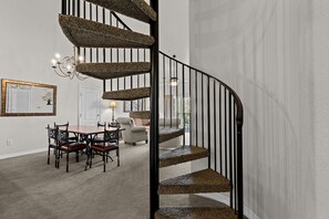 A spiral staircase with a textured carpet leading to a dining area with a table and chairs. - French Quarter | 2 King Bedrooms + Loft (Branson)