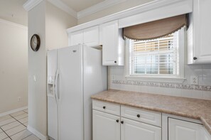 A kitchen with white cabinets, a refrigerator, a window with blinds, and a clock on the wall. - French Quarter | 2 King Bedrooms + Loft (Branson)