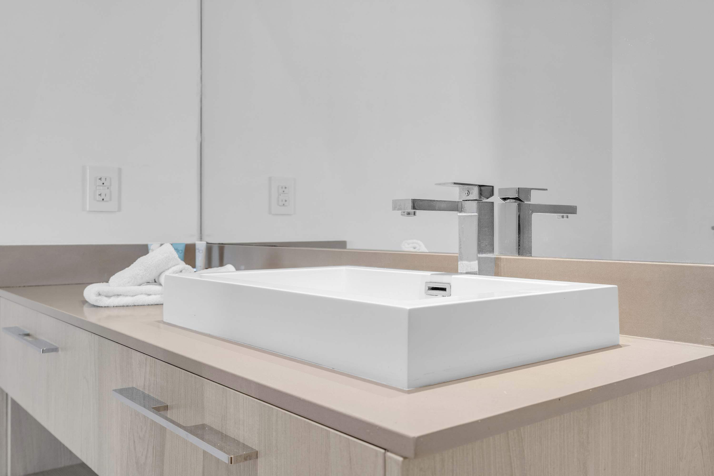 Une salle de bain moderne avec un lavabo blanc, un grand miroir et une serviette posée sur le comptoir.