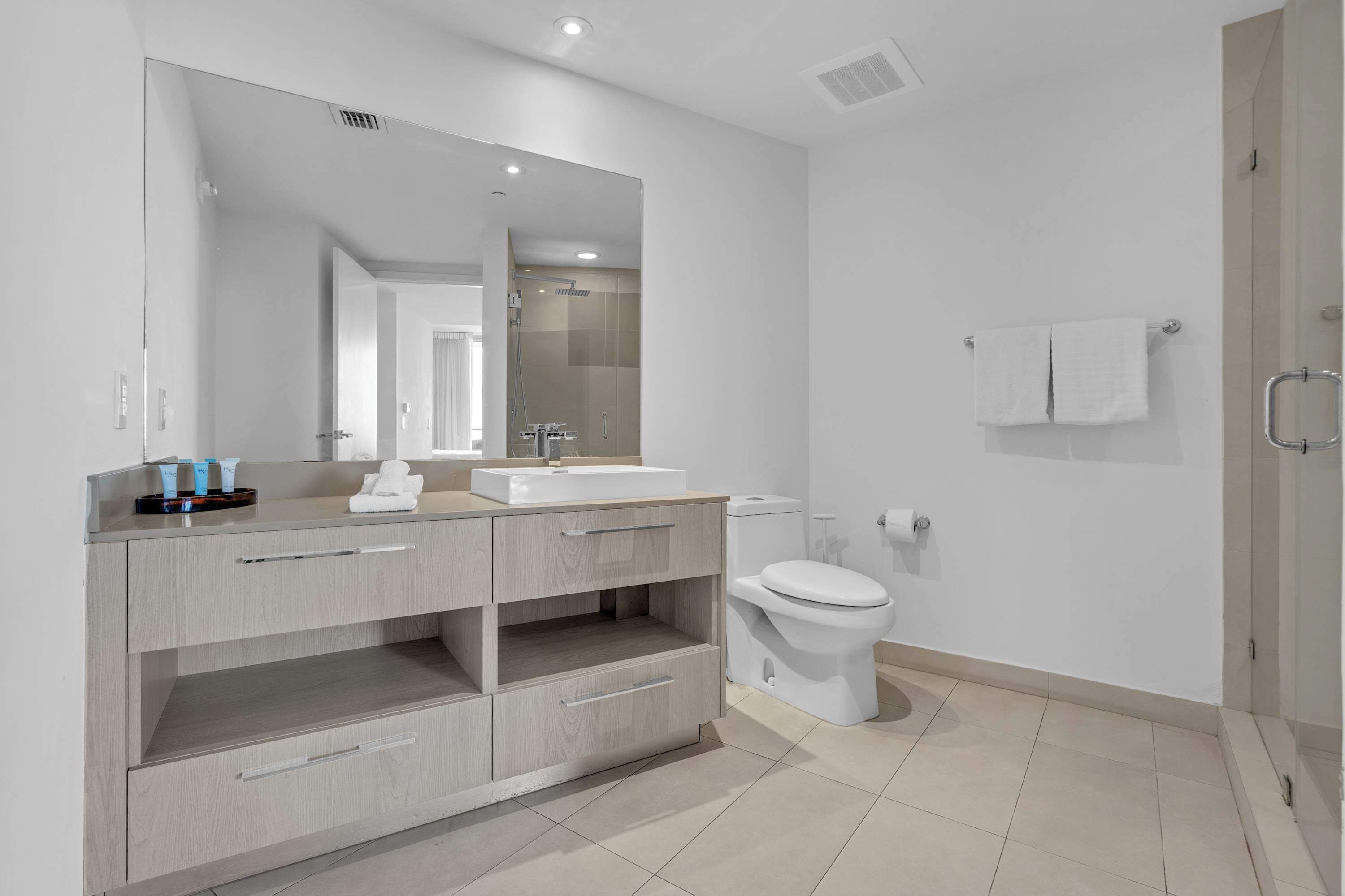 A modern bathroom with a large mirror, a sink, a toilet, and a shower area.