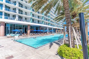 A hotel pool area with a clear blue pool, lounge chairs, umbrellas, and a palm tree. - Waterfront Oasis with Resort Amenities 6 people (Hollywood)