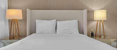 Una habitación de hotel con una cama grande, dos mesitas de noche con lámparas y un cabecero de madera.