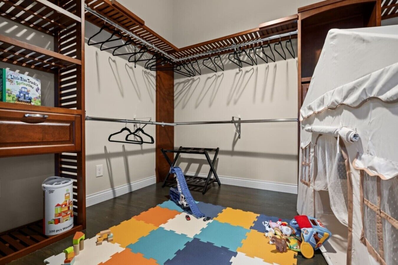 Una habitación con un estante de madera, un tendedero, una alfombra de juegos colorida y una cortina blanca.