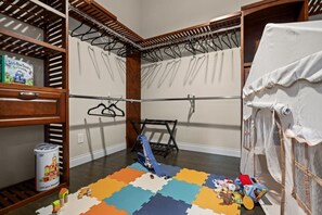 A room with a wooden shelving unit, a drying rack, a colorful play mat, and a white curtain.