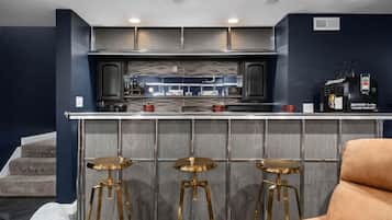 A modern kitchen with a bar area, featuring stainless steel appliances, a bar stool setup, and a visible refrigerator.