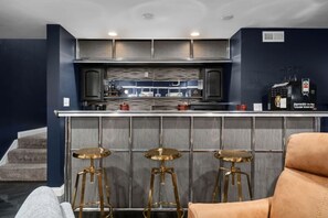 A modern kitchen with a bar area, featuring stainless steel appliances, a bar stool setup, and a visible refrigerator.