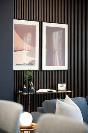Ein modernes Wohnzimmer mit einer Couch, einem Beistelltisch mit Lampe und zwei gerahmten Bildern an der Wand.