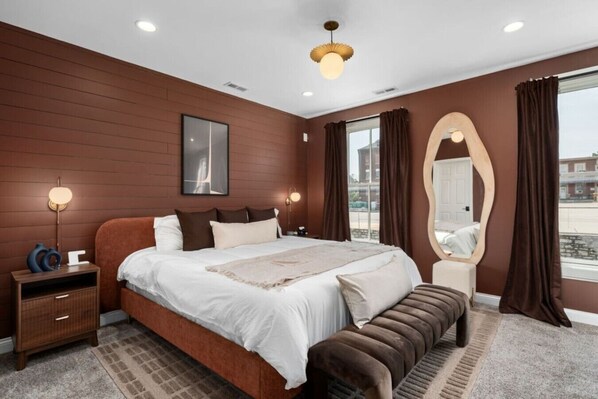 A modern bedroom with a large bed, bedside lamps, a mirror, and a view of the outside.