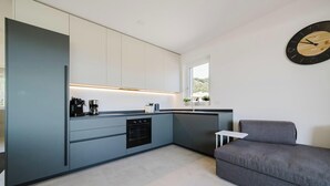 Eine moderne Küche mit Einbauofen, einer Kaffeemaschine und einer kleinen Essecke mit grauem Sofa.