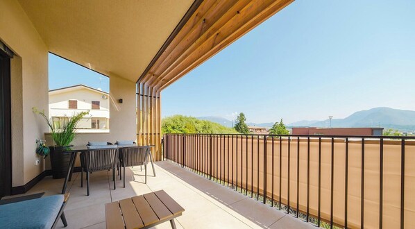 En balkon med et bord, stole, en bænk og udsigt til bygninger og bjerge.
