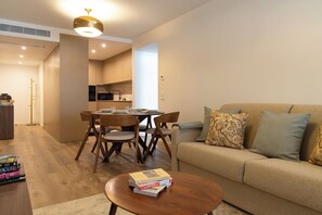 Ein modernes Wohnzimmer mit einer Couch, einem Couchtisch mit Büchern, einem Essbereich mit Stühlen und einem Tisch sowie einer Küche im Hintergrund.