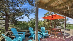 Un espacio de estar al aire libre con muelle de madera, sillas Adirondack azules, una mesa de picnic y un paraguas rojo.