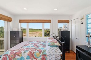 Ein Schlafzimmer mit Bett, Schminktisch und Blick auf ein Feld durch große Fenster.
