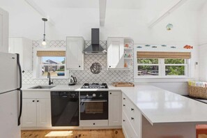 Une cuisine moderne avec des meubles blancs, un four encastré et une grande fenêtre offrant une belle vue.