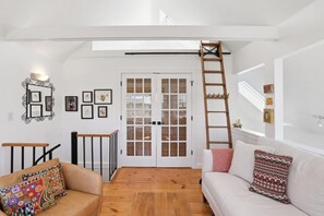 Ein Zimmer mit Holzboden, einem weißen Sofa, einem braunen Sofa, einer Treppe und einer Tür mit Glasverkleidung.