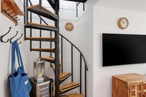 Una escalera de caracol con escalones de madera y barandillas de metal negro, un reloj en la pared y un televisor de pantalla plana.
