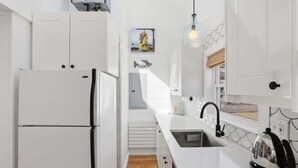 Una cocina moderna con armarios blancos, un lavamanos de acero inoxidable y una tetera sobre la encimera.