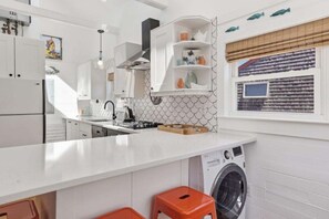 Eine moderne Küche mit weißen Schränken, einer integrierten Waschmaschine und einem Fenster mit Meerblick.