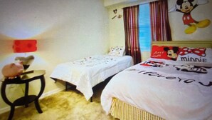 Habitación de hotel con dos camas, una mesita y una decoración de Mickey Mouse en la pared.