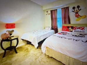 Ein Hotelzimmer mit zwei Betten, einem kleinen Tisch und einer Wanddekoration mit Mickey Mouse.