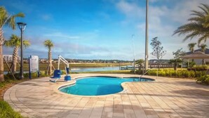 Una piscina de diseño curvo, rodeada por un solárium empedrado y palmeras.