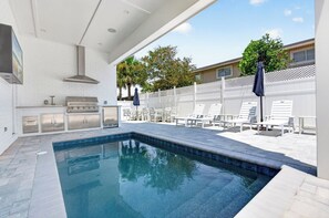 A swimming pool with a built-in grill and lounge chairs. - Serenity Shores: Private Beach, Ocean Views, Heated Pool, Golf Cart, Game Room (Miramar Beach)