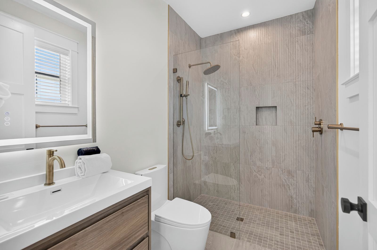 A modern bathroom with a glass-enclosed shower, a white sink with a gold faucet, and a toilet.