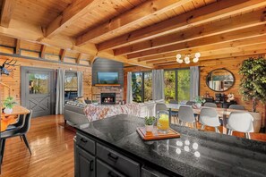 A modern log cabin interior with a kitchen, dining area, and living room. - Luxe Themed Cabin | Theater | Hot Tub | Mtn Views | Sleeps 18+ (Pigeon Forge)
