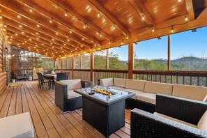 An outdoor deck with a glass-top fire pit, wicker furniture, and a view of the surrounding landscape. - Luxe Themed Cabin | Theater | Hot Tub | Mtn Views | Sleeps 18+ (Pigeon Forge)