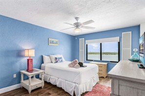A bedroom with a bed, bedside table, lamp, window, and a view of the outdoors. - Coastal Condo with Pool, Spa & Beach Fun Awaits - Condo Islands End 602 - Roelens (Fort Myers Beach)