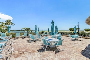 Eine Terrasse im Freien mit Tischen, Stühlen und Sonnenschirmen, mit Blick auf den Strand.