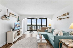 A living room with a sofa, coffee table, and a television. There is a balcony with a view. - Coastal Condo with Pool, Spa & Beach Fun Awaits - Condo Islands End 602 - Roelens (Fort Myers Beach)
