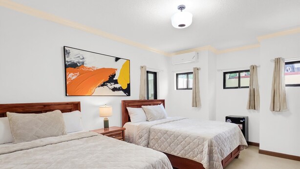 A hotel room with two beds, a painting on the wall, and an air conditioning unit. - Spacious 12 Bedrooms Villa for Large Groups in St Ann, Jamaica (Saint Ann's Bay)