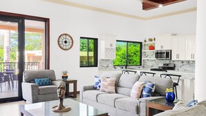 A modern living room with a sofa, coffee table, and a dining area with chairs. There is a kitchen with white cabinets and a microwave. - Spacious 12 Bedrooms Villa for Large Groups in St Ann, Jamaica (Saint Ann's Bay)