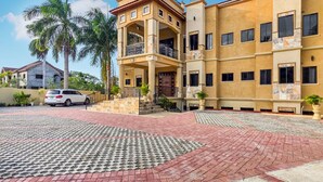 A multi-story residential building with a central courtyard, a white car parked in the driveway, and a palm tree. - Spacious 12 Bedrooms Villa for Large Groups in St Ann, Jamaica (Saint Ann's Bay)