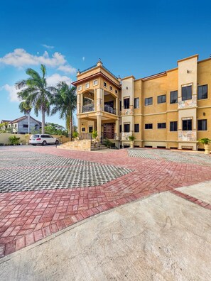 A multi-story residential building with a central courtyard, a white car parked in the driveway, and a palm tree. - Spacious 12 Bedrooms Villa for Large Groups in St Ann, Jamaica (Saint Ann's Bay)