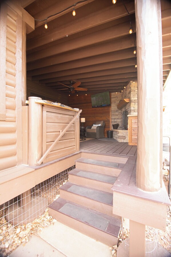 A wooden staircase leading to a covered porch area with a television mounted on the wall.