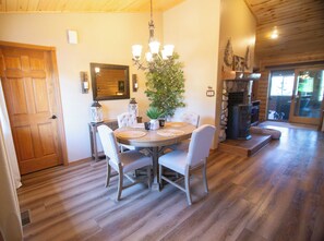 A dining area with a round table, chairs, a chandelier, and a fireplace.