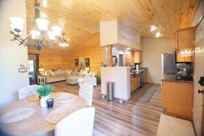 A modern interior with a dining area, kitchen, and living space, featuring wooden floors and a chandelier.