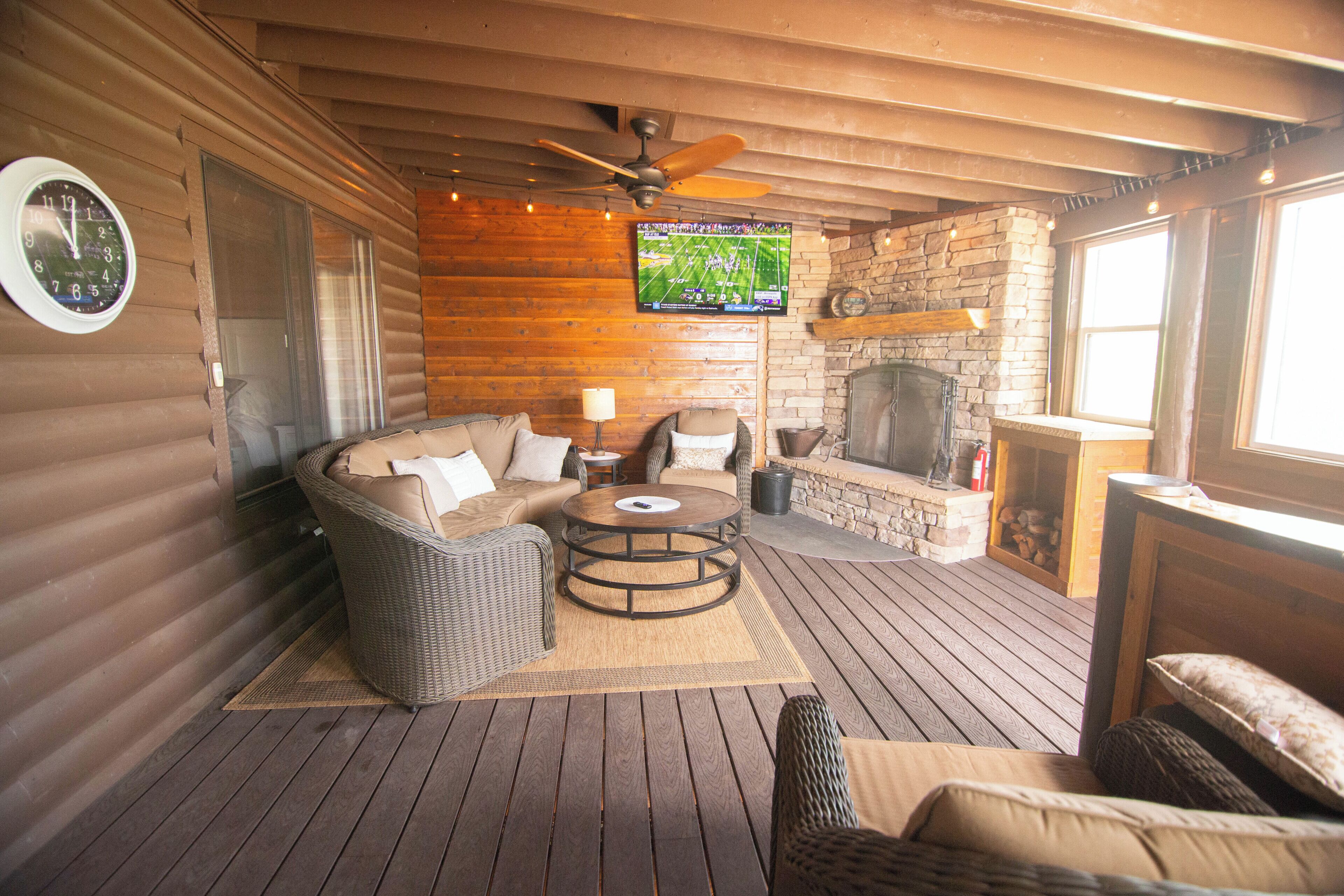 A cozy outdoor seating area with a sofa, chairs, and a round table, featuring a television screen above.