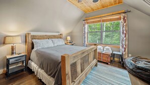 Ein Schlafzimmer mit einem Holzbett, einem Nachttisch, einer Lampe, einem Fenster mit Vorhängen und einem Deckenventilator.
