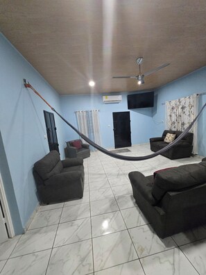 A living room with two sofas, a ceiling fan, a mounted TV, and a hammock.