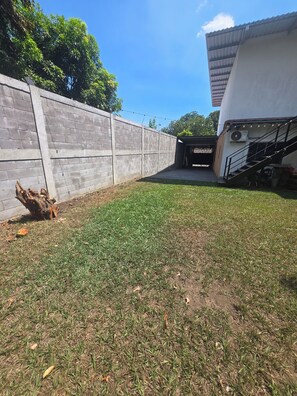 Un pati amb una paret de formigó, una zona verda i una escala que condueix a una construcció coberta.